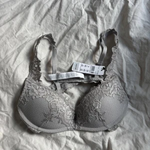 Grå spets-bh från intimissimi ny - Säljer en snygg grå bh från intimmissimimed vadderade kupor och vacker spetsdetalj över hela framsidan och axelbanden. Bh:n har justerbara axelband och en mjuk, bekväm känsla. Perfekt för dig som gillar stilrena underkläder med lite extra detalj. Den är helt ny och inte använda 