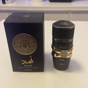 Lattafa Asad Parfym Svart & Guld - Lattafa Asad är en lyxig parfym i svart flaska med eleganta gulddetaljer och orientaliskt lejonmotiv. Flaskan har en unik form med dekorativa band och matchande svart och guldig förpackning. Perfekt för dig som gillar exklusiva dofter och snygg design. Tagit max 12 sprut med den.