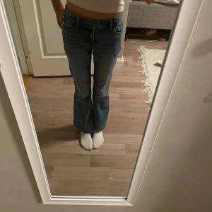 Blå bootcut jeans från Lindex - Snygga ljusblå bootcut jeans från Lindex med coola broderade detaljer och stjärna på bakfickan. Klassisk femficksmodell med låg midja och utsvängda ben. Perfekta för dig som gillar retro vibe och vill sticka ut lite extra.