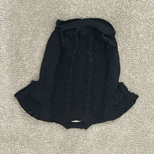 Svart blus med volangdetaljer - Säljer en svart blus med korta volangärmar och snyggt mönstrad framsida. Toppen har en feminin look med vågiga detaljer och lätt transparent tyg på vissa partier. Perfekt att styla med jeans eller kjol för en trendig outfit.