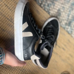 Svarta Veja sneakers i skinn, strl 37 - Snygga svarta Veja sneakers i skinn med vita detaljer och klassisk V-logga på sidan. Skorna har svarta snören, vit platt sula och rund tå. Perfekta för dig som gillar stilrena och trendiga sneakers med en clean look.