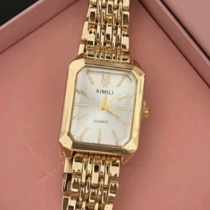 Guldig fyrkantig klocka  - Stilren klocka  med fyrkantig urtavla i vitt och länkarmband i guld. Klockan har en elegant design med tydliga markeringar och quartz-urverk. Perfekt accessoar för att lyfta din outfit.Box i går ej.