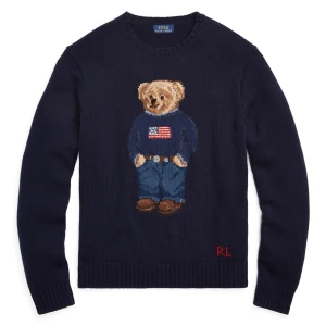 Mörkblå stickad tröja Polo Bear - Säljer en mörkblå stickad tröja från Ralph Lauren med ikoniska Polo Bear-motivet framtill. Tröjan har RL-broderi i rött vid nederkanten och ribbade muddar. Perfekt för dig som gillar klassisk stil med en twist och vill sticka ut lite extra.
