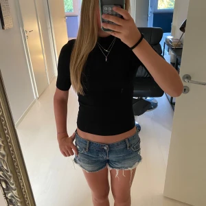 Svart ribbad topp från Zara - Svart ribbad topp från Zara med hög hals och korta ärmar. Sitter tight och har en croppad passform som passar perfekt till jeans eller kjol. Enkel och stilren design som är lätt att matcha med smycken eller lager på lager. Använd bara några få gånger! 