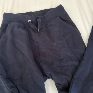 Mörkblå mjukisbyxor från 157 - Säljer ett par mörkblå mjukisbyxor från 157 med ribbad midja och snörning. Byxorna har en loose passform och är gjorda i mjukt bomullsmaterial, perfekta för chill dagar eller träning. Klassisk stil utan mönster eller extra detaljer.