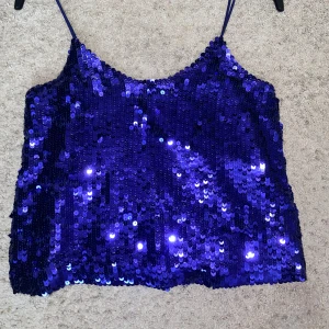 Blå paljett-topp med smala band - Glittrig blå topp täckt av paljetter med smala axelband. Croppad modell som verkligen sticker ut och passar perfekt när du vill synas. Snygg att styla med jeans eller kjol för en cool look.