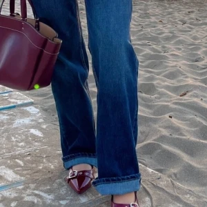 Vinröda ballerinaskor med spännen - Snygga ballerinaskor i vinrött lack med två breda remmar och silvriga spännen. Skorna har spetsig tå och coola metalldetaljer som ger en edgy vibe. Perfekta att styla med jeans eller kjol för en trendig look.