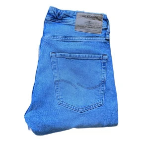 Jack & Jones Jeans - Säljer ett par klassiska ljusblå jeans från Jack & Jones. Jeansen har rak passform, fem fickor och snygga kontrastsömmar. Tillverkade i bomull med en skön jeanskänsla. Perfekta för dig som gillar en enkel och tidlös look. Längd 98cm Jag skickar ej bild när jag bär plaggen och jag vet ej vilken längd och vikt de passar då jag inte prövar kläderna jag säljer 😃