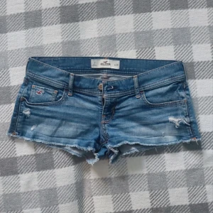 Blå jeansshorts från Hollister - ❣️Intressekoll!! ❣️Snygga blå jeansshorts från Hollister med slitna detaljer och råa kanter. Klassisk femficksmodell med låg midja och logga på fickan. Perfekta för varma dagar och en avslappnad stil. Skriv vad ni kan tänka er betala 🥰