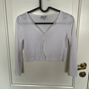 Vit croppad blus från Madlady - Säljer en vit croppad blus från Madlady med v-ringning och långa ärmar. Toppen har knappar framtill och är i ett tunt, lätt material som känns skönt mot huden. Perfekt att styla med jeans eller kjol för en clean look.