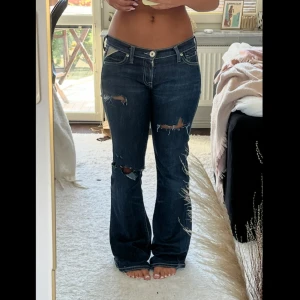 Lågmidjade bootcut jeans från Replay - Säljer ett par lågmidjade mörkblå bootcut jeans från Replay med slitna detaljer och hål på benen. Jeansen är köpta secondhand men efter det bara använda två gånger. Storlek W 28,L 32