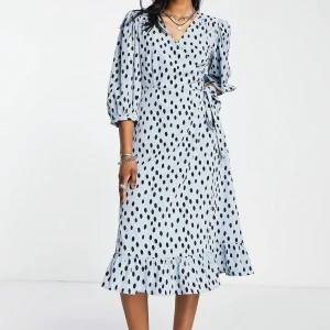 Ljusblå prickig omlottklänning - Ljusblå omlottklänning med svarta prickar och trekvartsärmar. Klänningen har knyt i midjan och v-ringning, vilket ger en avslappnad men trendig look. Använd max 2 gånger, osäker på storlek men passar för L/XL. Nypris 600kr