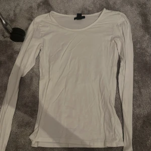 Vit långärmad basic tröja - Enkel och stilren vit långärmad tröja med rund halsringning. Perfekt som basplagg och lätt att matcha med olika outfits. Tröjan är i ett mjukt och tunt material som känns skönt mot huden.