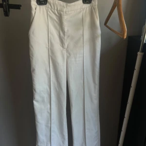 Vita kostymbyxor Misslisibell x NA-KD - Snygga vita kostymbyxor från Misslisibell x NA-KD. Byxorna har raka ben, pressveck framtill och två fickor bak. Perfekta för en clean och stilren look. Tillverkade i ett mjukt bomullsmaterial.