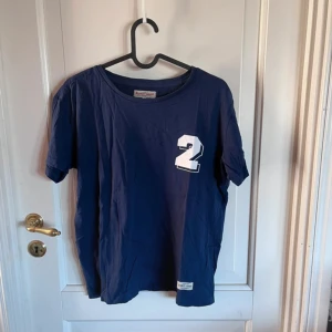 Mörkblå t-shirt Iconic Sport med tryck - Mörkblå t-shirt från Iconic Sport i 100% bomull. Klassisk passform med rund hals och korta ärmar. På bröstet finns en vit siffra 2 som tryck. Perfekt basic-plagg med sportig vibe och enkel stil.