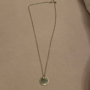 Enkelt guldhalsband med rund berlock - Stilrent halsband i guld med en tunn kedja och en rund, slät berlock. Perfekt för dig som gillar minimalistiska smycken och vill ha något som funkar till allt. Berlocken har en spegelblank finish som fångar ljuset snyggt.💕🤗