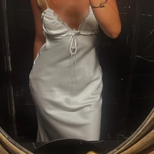Vit klänning i satin - Supersnygg vit långklänning i satin med tunna axelband och v-ringning, super fin rygg. Snörningsdetalj framtill och lätt volangkant. Från Zara. Perfekt för sommarens alla tillfällen när du vill känna dig extra fin.