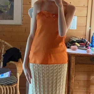 Orange satinlinne med spetsdetalj - Snygg orange linnetopp i satin med tunna axelband och spetsdetalj längs urringningen. Toppen har en lätt glansig finish och en rak, något lös passform. Perfekt för dig som vill sticka ut med färg och coola detaljer.