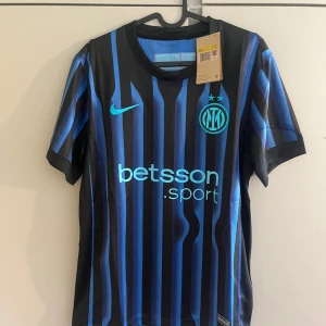 Inter Milan randig fotbollströja Nike - Snygg Inter Milan fotbollströja från Nike med klassiska svarta och blå ränder. Tröjan har korta ärmar, rund hals och klubbmärke samt Nike-logga på bröstet. Tillverkad i lätt och ventilerande material, perfekt för match eller träning.