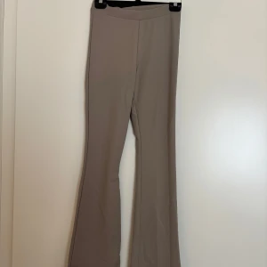 Beiga bootcut byxor från 157 - Snygga beiga bootcut-byxor från 157 i stretchigt material. Byxorna har hög midja och en stilren, minimalistisk look utan synliga fickor eller detaljer. Perfekta för dig som gillar en clean och trendig vibe.