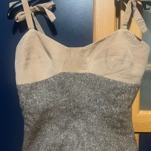 Vintage topp från Tara Jarmon - Säljer en unik vintage topp från Tara Jarmon i storlek 36 (mer som 34). Den har en beige färg med ljusare prickar på övre delen av toppen, sedan knytsnören som axelband. Underdelen av toppen är gråmelerad med mix av olika färger. Det är olika material på delarna. Sparsamt använd och inga defekter.