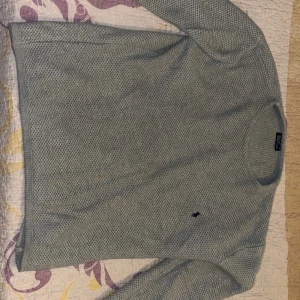 Grå stickad tröja från Polo Ralph Lauren - Snygg grå stickad tröja från Polo Ralph Lauren med diskret svart logga broderad på bröstet. Tröjan har rund halsringning och långa ärmar, perfekt för lager-på-lager-stil under kyliga dagar.