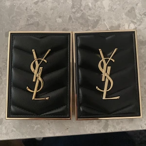 YSL ögonskuggspaletter & läppstift - Två lyxiga YSL ögonskuggspaletter med fyra nyanser i varje, i varma nude och rosa toner. Tre YSL Rouge Pur Couture The Bold-läppstift i svarta och guldiga hylsor (nyans 13 & 14 synliga) samt ett silvrigt YSL-läppstift med rosa detalj. Snygg design med YSL-logga. Man kan också köpa en sak 