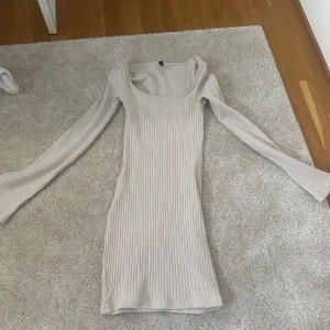 Ribbad vit kortklänning från H&M Divided - Supersnygg ribbad vit kortklänning från H&M Divided. Klänningen har lång ärm, tight passform och rundad urringning. Perfekt för dig som gillar en enkel men trendig stil. Materialet är mjukt och stretchigt, vilket gör den riktigt bekväm.