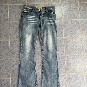 Bootcut jeans från Cocolulu - Snygga blå bootcut jeans från Cocolulu med slitningar och ljusa partier framtill. Låg midja och klassisk femficksmodell. Jeansen har en cool vintagekänsla och är tillverkade i denim med stretch. Perfekta för dig som gillar 00-talsstil.