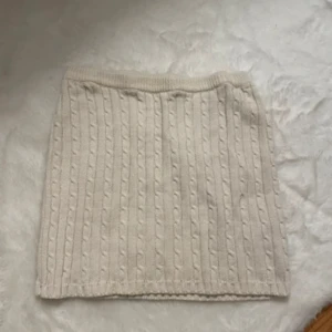 Stickad beige kortkjol - Superfin stickad beige kortkjol med kabelstickat mönster. Kjolen har en mjuk och skön känsla och passar perfekt till en mysig outfit. Enkel att matcha med både boots och sneakers.