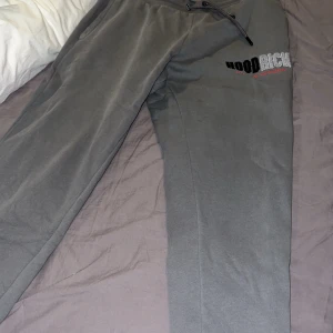 Grå mjukisbyxor från Hoodrich M - Snygga grå mjukisbyxor från Hoodrich i storlek M. Byxorna har resår och snörning i midjan, ribbade muddar vid bensluten och Hoodrich-logga broderad på ena benet. Perfekta för chill eller streetwear vibes.