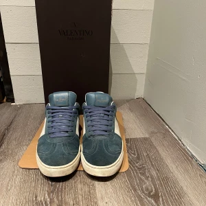Valentino Flycrews - Valentino Garavani i blå mocka med vita skinnpaneler och blå snörning. Strlk 42 passar också dom som har 43. Skorna har rund tå, platt sula med coolt kamouflagemönster undertill och diskreta nitar vid hälen. Två nitar på hälarna är av så 4 st totalt, jag har suttit på 3 st nitar själv, det är lite heeldrag på skorna också som man kan se på bild 4 men inget värre. Vad tillkommer? Valentino box, 2 st nitar, 2st dustbags och ett par extra snören. Boxen är lite paj i hörnet. Öppen för byten!