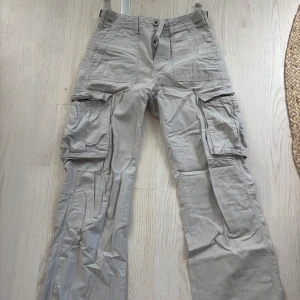 Beiga cargo byxor från Bershka - Säljer ett par beiga cargobyxor från Bershka med raka ben och flera stora fickor på sidorna. Perfekta för en avslappnad  look. Byxorna har inte använts på länge och är därför skrynkliga men bortsett från det är dom i ett mycket bra skick.