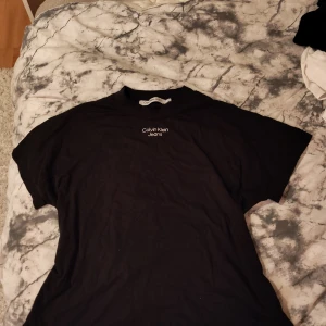 Svart Calvin Klein Jeans t-shirt - Svart t-shirt från Calvin Klein Jeans med vit logga tryckt på bröstet. Klassisk rund hals och korta ärmar. Tillverkad i 100% bomull för en skön och avslappnad känsla. Perfekt till jeans eller shorts för en clean look.