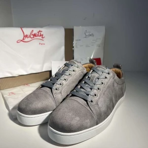 Grå mockasneakers från Louboutin - Snygga grå sneakers från Louboutin i mjuk mocka med klassisk röd sula och vita kanter. Skorna har rund tå, platt sula och grå snörning. Insidan är fodrad i beige skinn för extra komfort. Perfekta för dig som gillar stilrena och exklusiva sneakers.
