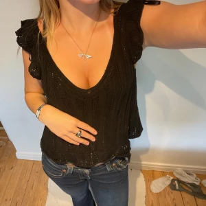 Svart stickad topp från ONLY - Supersöt svart virkad topp från ONLY med v-ringning och volangdetaljer vid axlarna. Toppen är ärmlös och har en luftig, virkad känsla som passar perfekt till jeans eller kjol. Snygg och enkel att styla för en trendig look.