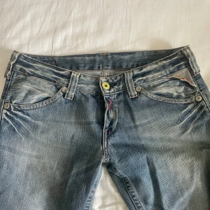 Replay jeans low waist blå W29 L32 - Säljer ett par blå Replay jeans med låg midja och raka ben. Jeansen har slitna detaljer, ljus tvätt och coola gula detaljer vid knappen och bakfickorna. Klassisk femficksmodell i jeansmaterial, perfekt för en avslappnad streetstil.
