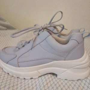 Chunky ljuslila sneakers med platåsula - Säljer ett par chunky sneakers i ljuslila med kraftig vit platåsula. Skorna har snörning och rund tå, samt detaljerade sömmar och dragflik bak. Perfekta för dig som gillar en sportig och trendig look.