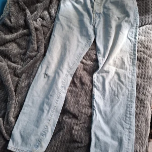 Ljusblå raka jeans, W29 L32 - Midja till fot: 107cm. Midja till midja: 42cm. Ljusblå jeans med rak passform och klassisk femficksdesign. Jeansen har slitna detaljer vid benslut och ett hål på ena benet för en avslappnad vibe. Perfekta för dig som gillar en vintagekänsla och vill ha ett par sköna, raka jeans i bomull.
