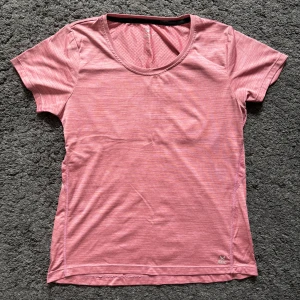 Rosa träningst-shirt från SOC - Sportig rosa t-shirt från SOC med diskret mönster och rund hals. Tillverkad i lätt och ventilerande syntetmaterial, perfekt för träning. Kortärmad modell med reflekterande detalj på ryggen för extra synlighet.