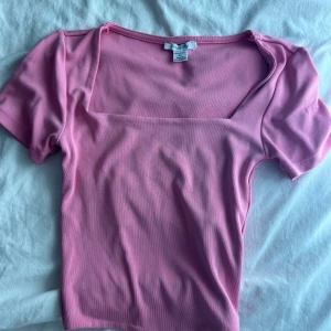 Rosa topp med fyrkantig ringning Amisu - Säljer en söt rosa topp från Amisu i storlek XS. Toppen har en snygg fyrkantig ringning och korta ärmar. Materialet är mjukt och stretchigt, perfekt för en trendig och bekväm look. Passar dig som gillar färg och enkel stil.