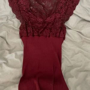 Vinröd spetslinnetopp från Rosemunde - Vinröd tajt linnetopp från Rosemunde med breda spetsaxelband och u-ringning. Överdelen är i blommig spets och nederdelen är ribbad, använd 2 gånger!! Toppen ser röd ut på bilderna men är vinröd i verkligheten