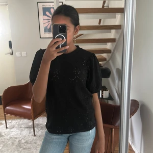 Svart blus med broderade detaljer - Svart blus från vila med korta puffärmar och broderade hålmönster över hela tyget. Blusen har en rund halsringning och är tillverkad i ett lätt material som ger en luftig känsla. Perfekt för dig som gillar stilrena men ändå unika plagg.