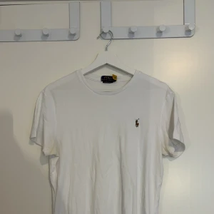 Vit t-shirt Polo Ralph Lauren - Vit t-shirt från Polo Ralph Lauren med klassisk broderad logga på bröstet. Modellen är custom slim fit med korta ärmar och rund hals. Tillverkad i mjuk bomull, perfekt för en clean och stilren look.