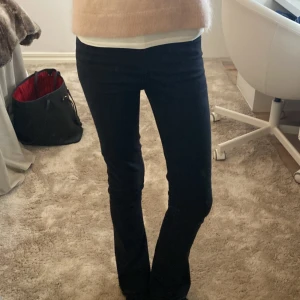 Svarta bootcut jeans mid waist - Snygga svarta jeans med bootcut-modell och hög midja. Jeansen har klassisk femficksdesign, dragkedja och knapp framtill. Materialet är stretchigt och sitter tajt upptill med utsvängda ben. Perfekta för dig som gillar en stilren och trendig look. Har sprättat upp vid byxänden men inget man tänker på