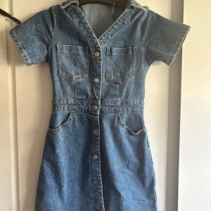Kort jeansklänning från zara  - Snygg kort jeansklänning med v-ringning, korta ärmar och knappar hela vägen framtill. Klänningen har två bröstfickor, två sidfickor och två bakfickor. Perfekt för dig som gillar en avslappnad och cool stil.