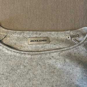 Ljusgrå stickad tröja Jack & Jones - En stilren ljusgrå stickad tröja från Jack & Jones i storlek S. Tröjan har rund halsringning, lång ärm och diskret logga nertill. Perfekt för lager-på-lager och enkel att matcha med jeans eller chinos. PRIS KAN SJÄLVKLART DISKUTERAS 