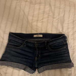 Mörkblå jeansshorts från Hollister - Snygga mörkblå jeansshorts från Hollister med klassisk femficksdesign och uppvikta benslut. Shortsen har kontrastsömmar och bakfickor med broderade detaljer. Perfekta för varma dagar och enkel att matcha med allt. Pris kan diskuteras 😊