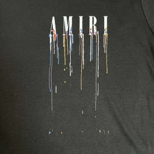 Svart AMIRI t-shirt med ängeltryck - Svart t-shirt från AMIRI i mjuk bomull med färgstänk och stor vit ängelgrafik på ryggen. Framsidan har AMIRI-logga med färgdrip-effekt. Klassisk passform och korta ärmar, perfekt för dig som gillar streetwear med konstnärlig vibe.