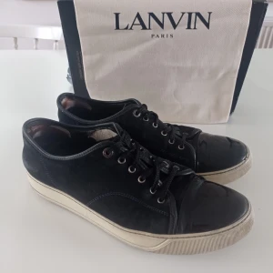 Svarta sneakers från Lanvin i mocka - Snygga svarta sneakers från Lanvin med ovandel i mocka och lackad tå. Skorna har vita gummisulor och klassisk snörning. Perfekta för dig som gillar stilrena och exklusiva sneakers med en twist.